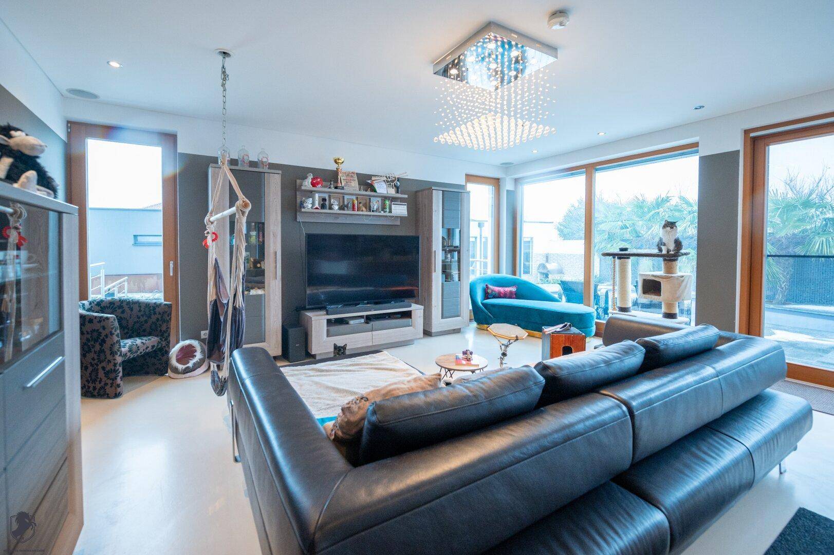 Lichtdurchflutetes Wohnzimmer mit gemütlichem Sofa, modernem Unterhaltungssystem und großen Fenstern mit Ausblick.