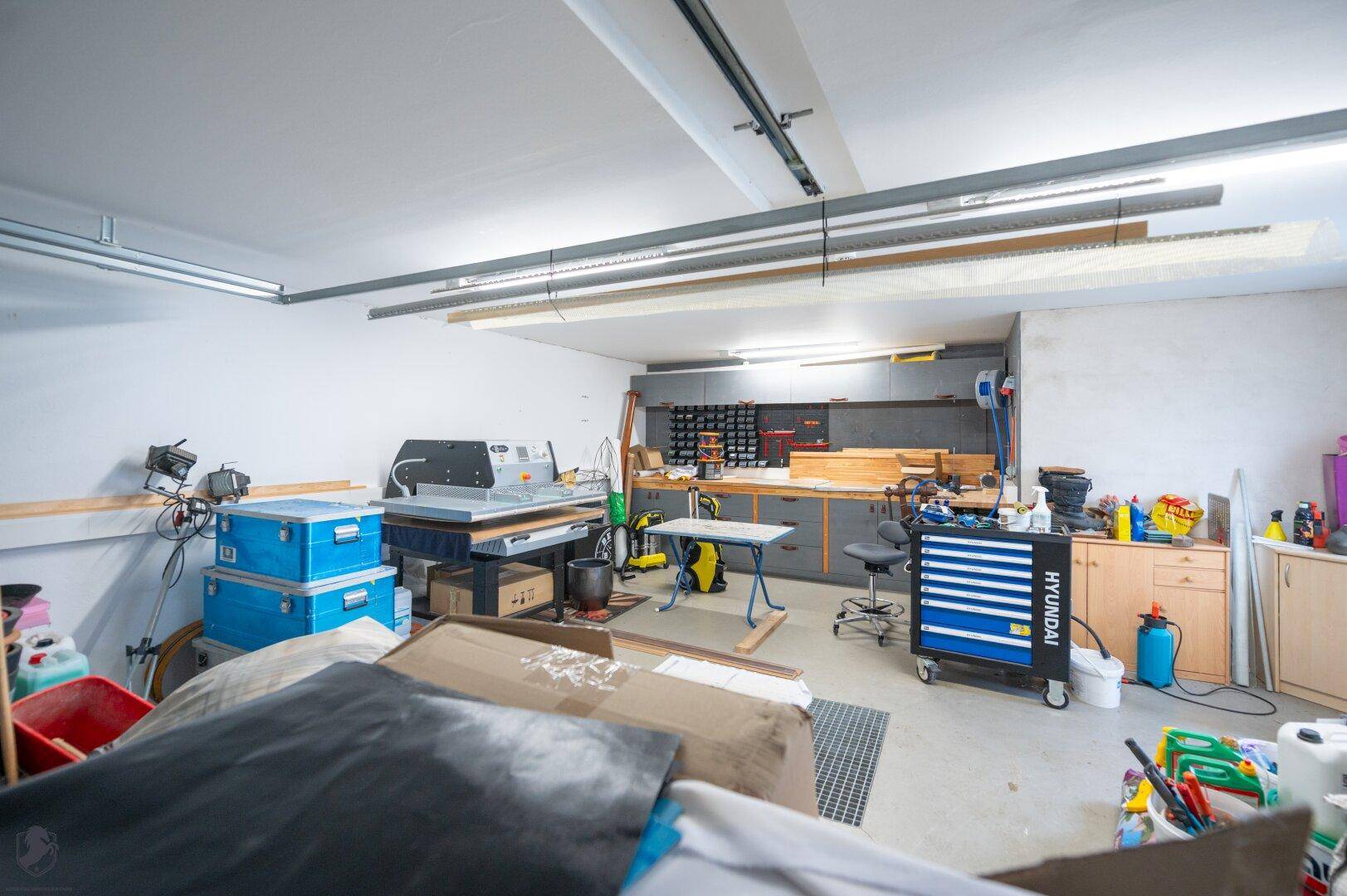 Gut ausgestattete Werkstatt in der Garage mit umfangreicher Arbeitsfläche und verschiedenen Aufbewahrungssystemen.