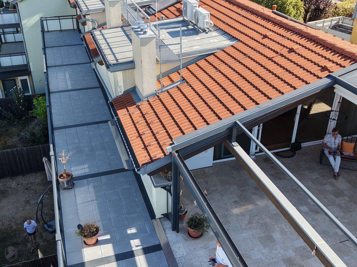 Vogelperspektive auf die Dachterrasse mit Sitzgelegenheiten und angrenzendem Ziegeldach.