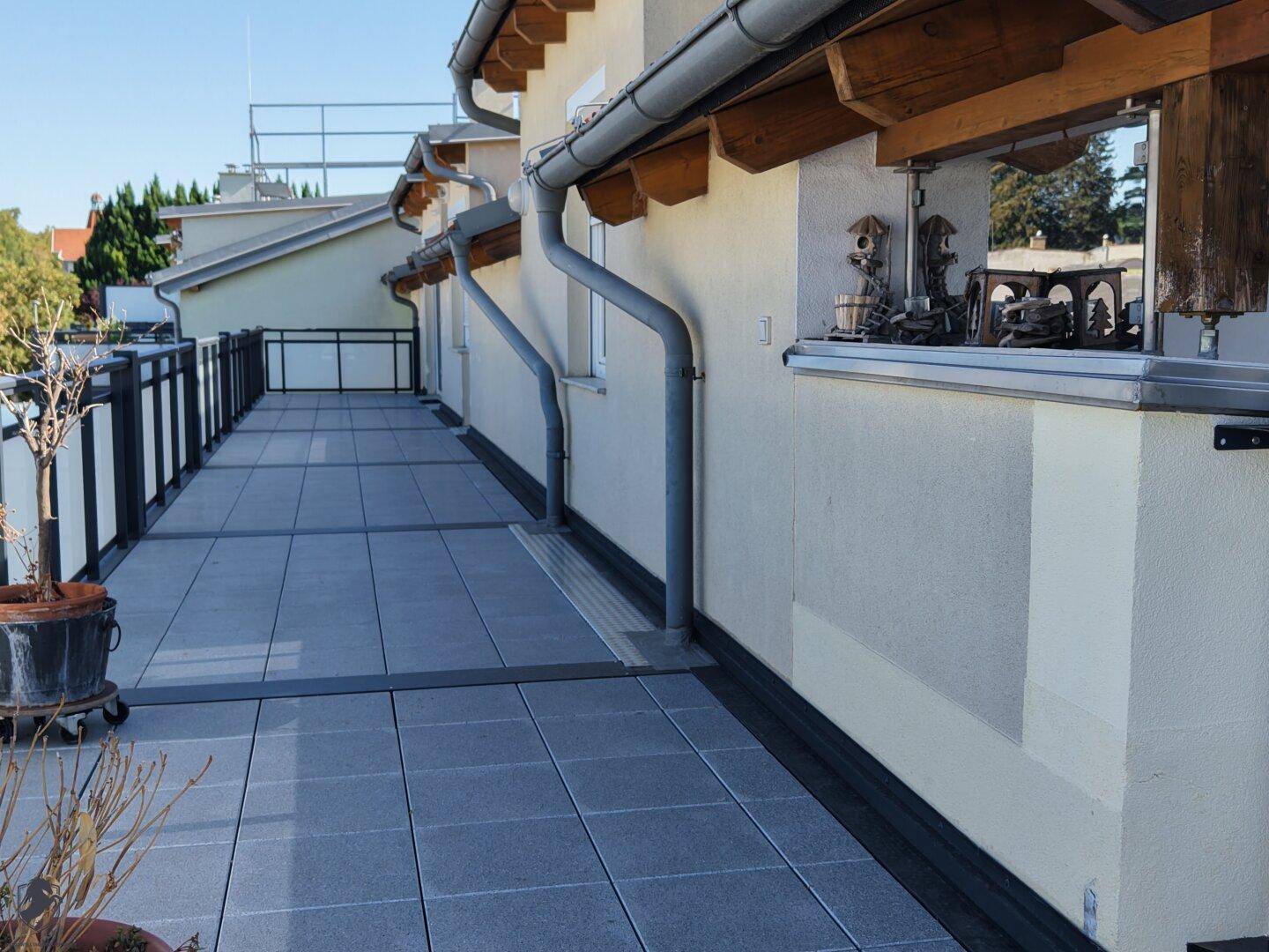 Langer, schmaler Terrassenbereich mit grauen Fliesen und Metallgeländer entlang der Hauswand.