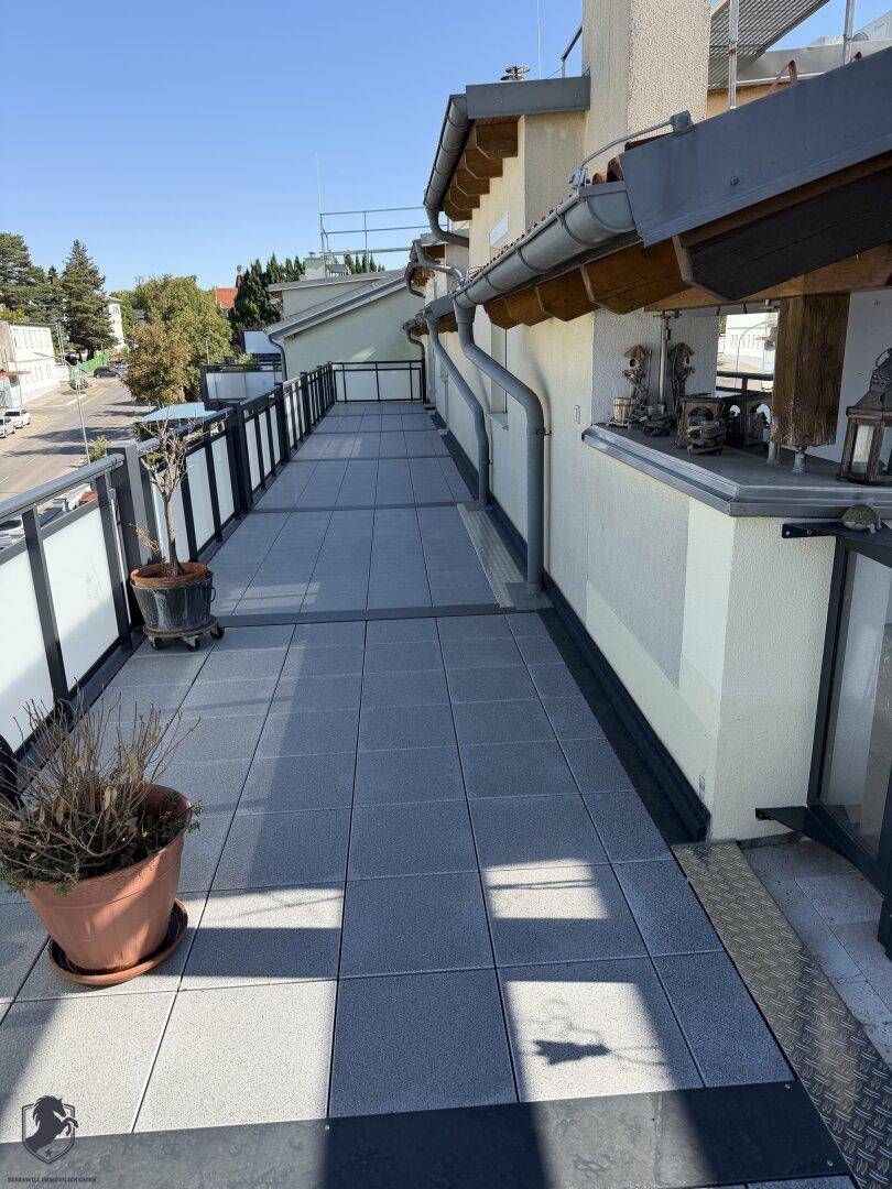 Schmaler Terrassenbereich mit grauen Fliesen und modernem Geländer, ideal für Pflanzen.