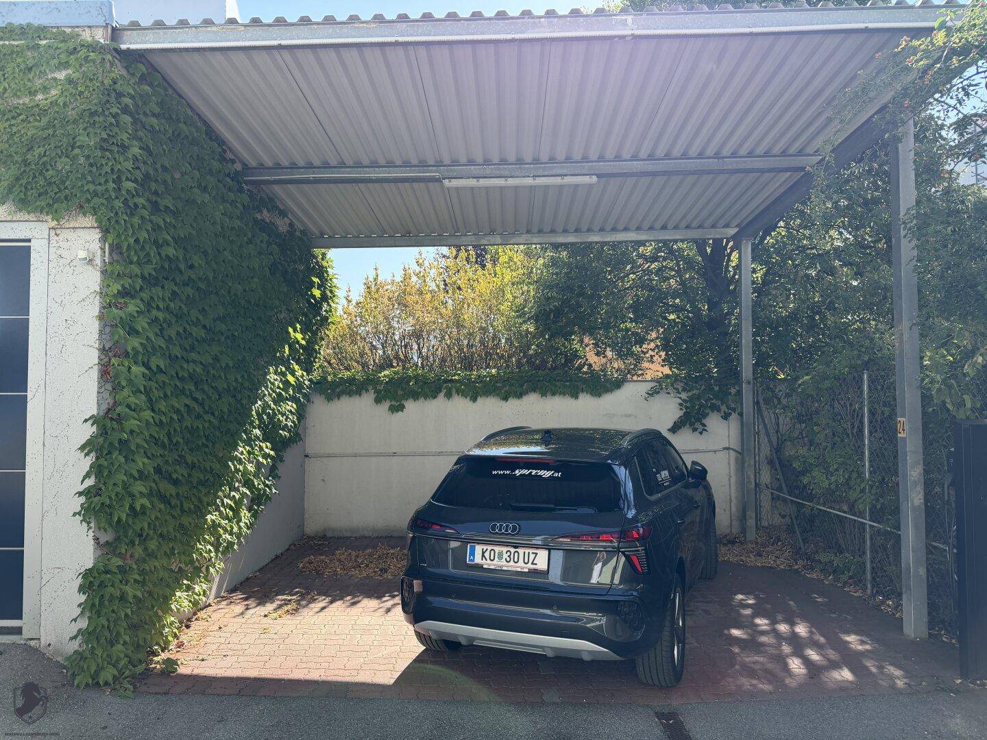 Überdachter Stellplatz (Carport) mit Efeu bewachsener Wand und geparktem Fahrzeug.
