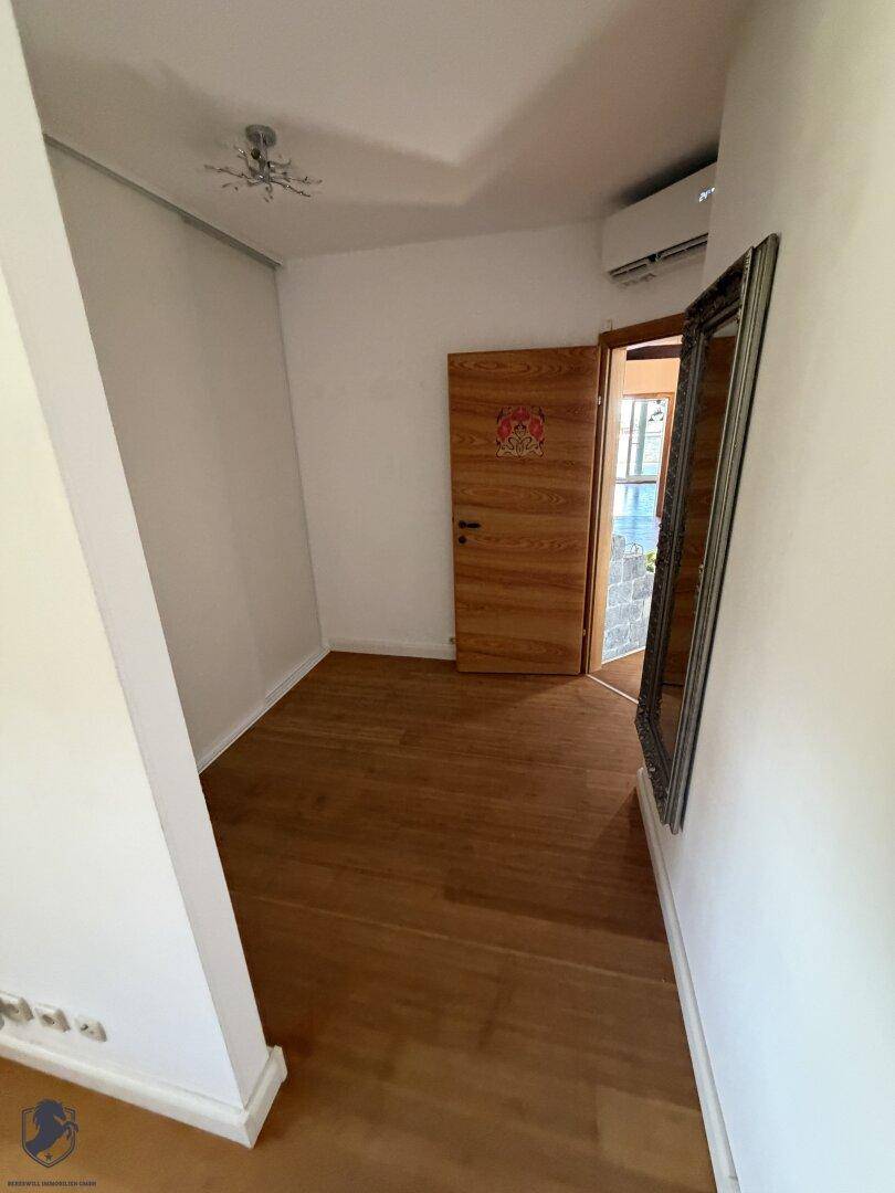 Kleiner Raum mit Holzboden, weiß gestrichenen Wänden und einem großen Spiegel.