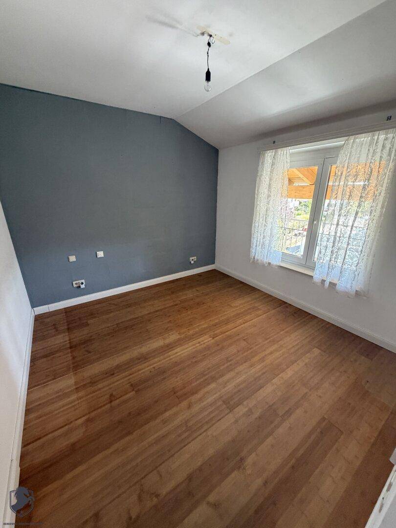 Schlafzimmer mit Holzboden, einer blauen Akzentwand und einem Fenster mit Vorhängen.