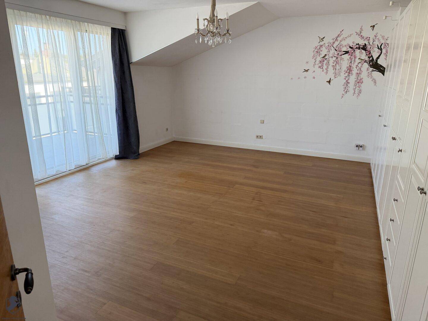 Geräumiges Schlafzimmer mit Holzboden, Dachschräge und Zugang zu einem Balkon oder einer Terrasse.