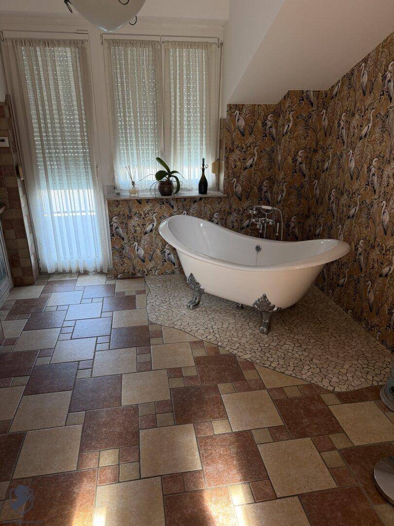 Badezimmer mit freistehender Badewanne, Fliesenboden und dekorativer Tapete an den Wänden.