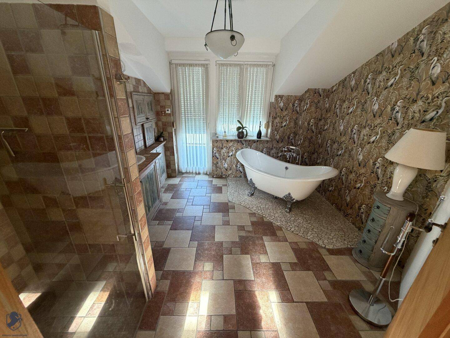 Geräumiges Badezimmer mit Duschbereich, freistehender Badewanne und großen Fenstern.