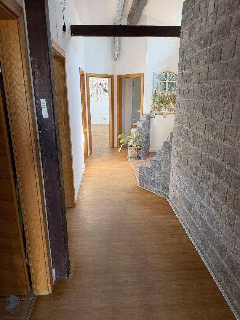 Geräumiger Flur mit Holzboden, sichtbaren Holzbalken und einer Steintreppe.
