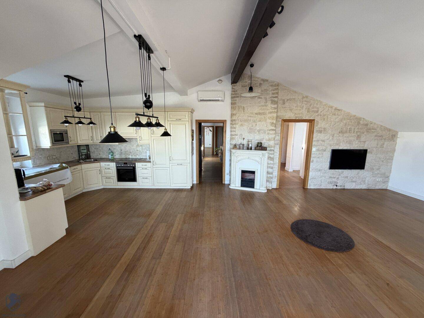 Offener Wohnbereich mit integrierter Küche, Holzboden und Dachschrägen, inklusive Kamin und TV-Wand.