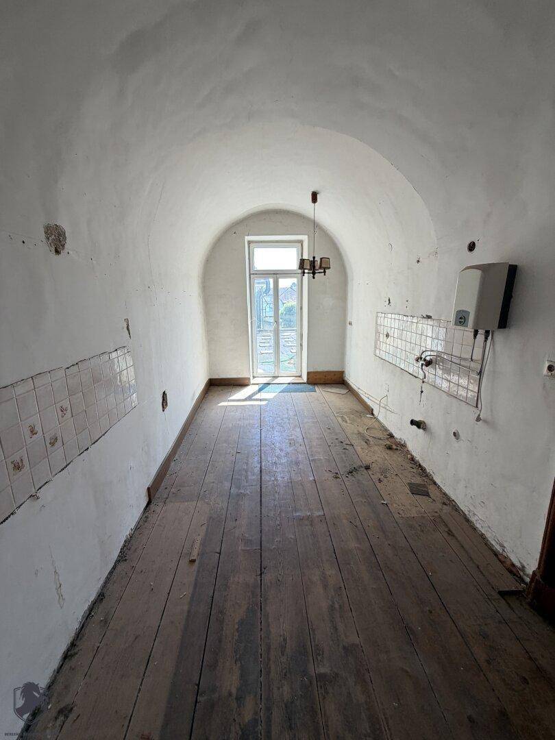 Lange, schmale Küche mit Holzboden, gewölbter Decke und einem Fenster am Ende des Raumes.