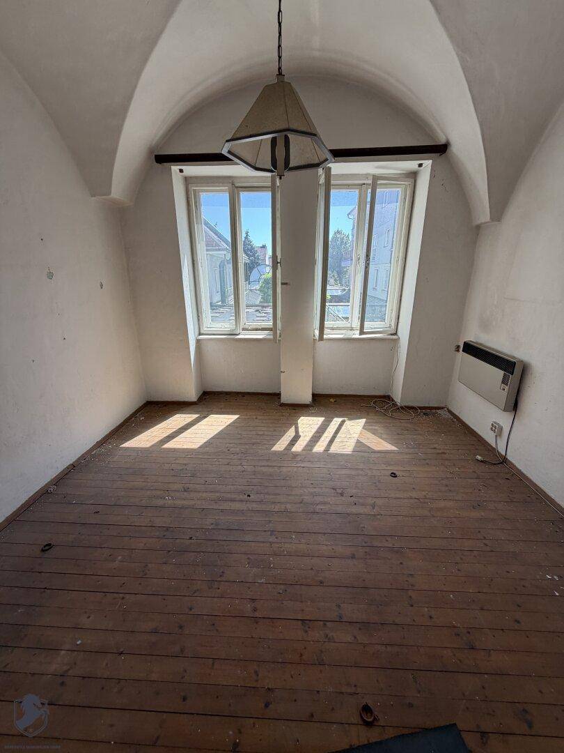 Heller Raum mit Holzboden, hohen Fenstern und einer markanten Gewölbedecke.