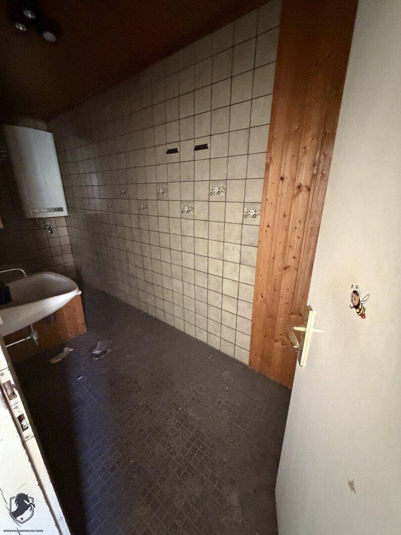 Kleines Badezimmer mit Fliesen an den Wänden, Waschbecken und Warmwasserbereiter.