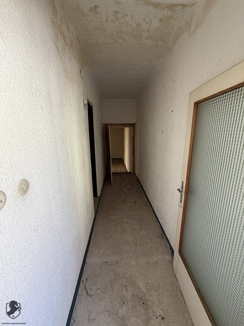 Langer, schmaler Flur mit weiß gestrichenen Wänden und Türen zu angrenzenden Räumen.
