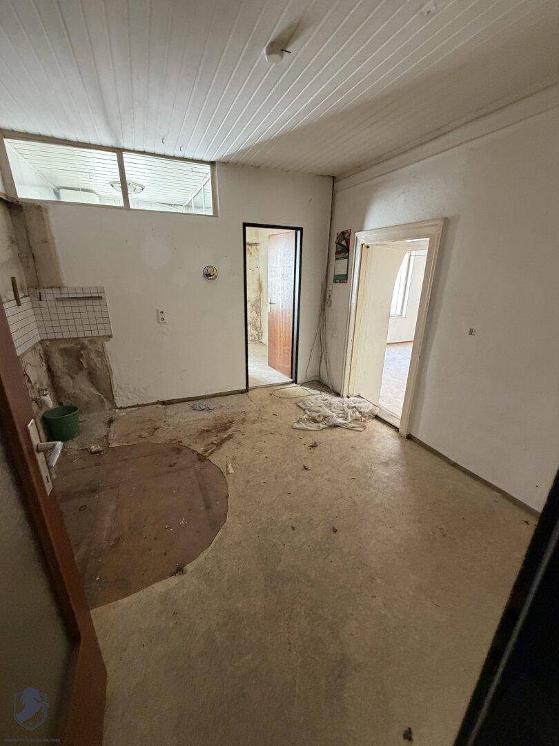 Leerer Raum mit teilweise gefliesten Wänden und sichtbaren Installationen, bereit zur Neugestaltung.