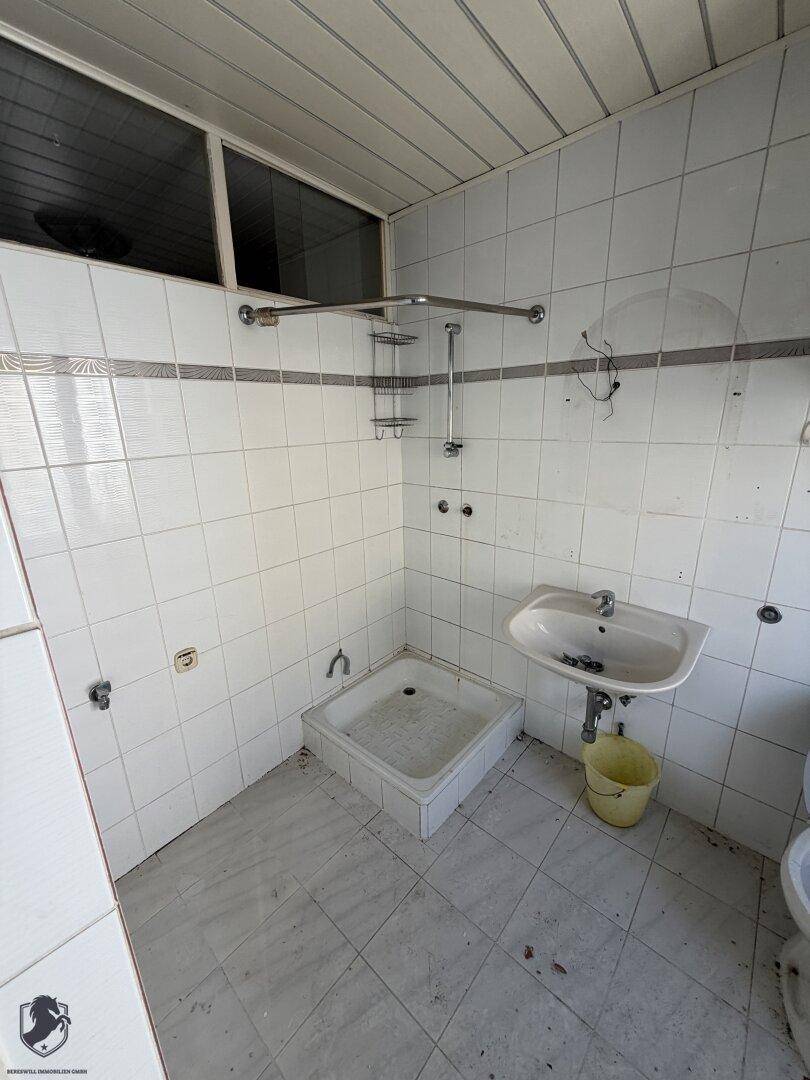 Badezimmer mit weißen Fliesen, Duschwanne und Waschbecken, renovierungsbedürftig.