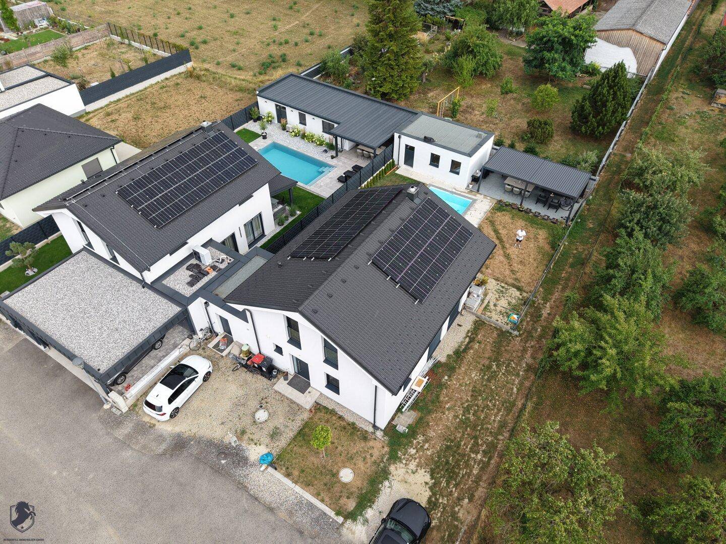 Luftaufnahme von zwei modernen Häusern mit Pools, Terrassen und Photovoltaikanlagen in ländlicher Umgebung.