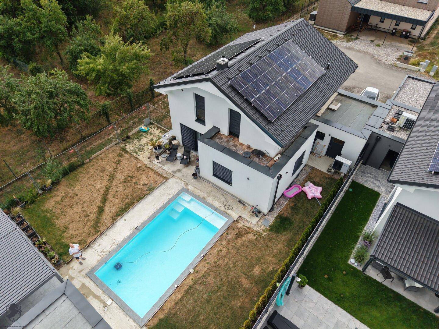 Hinterhof mit modernem Swimmingpool, Rasenfläche und Photovoltaikanlage auf dem Dach des Hauses.