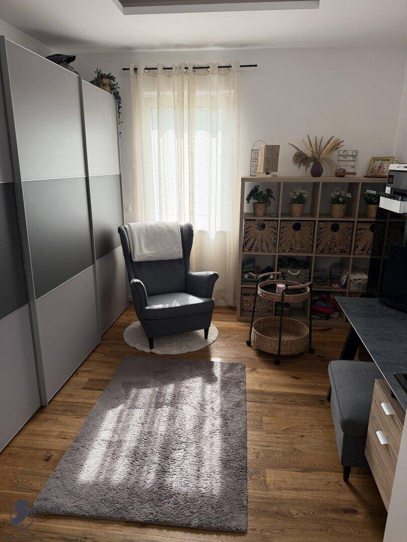 Gemütliches Schlafzimmer mit Holzfußboden, großem Kleiderschrank und einem bequemen Sessel am Fenster.