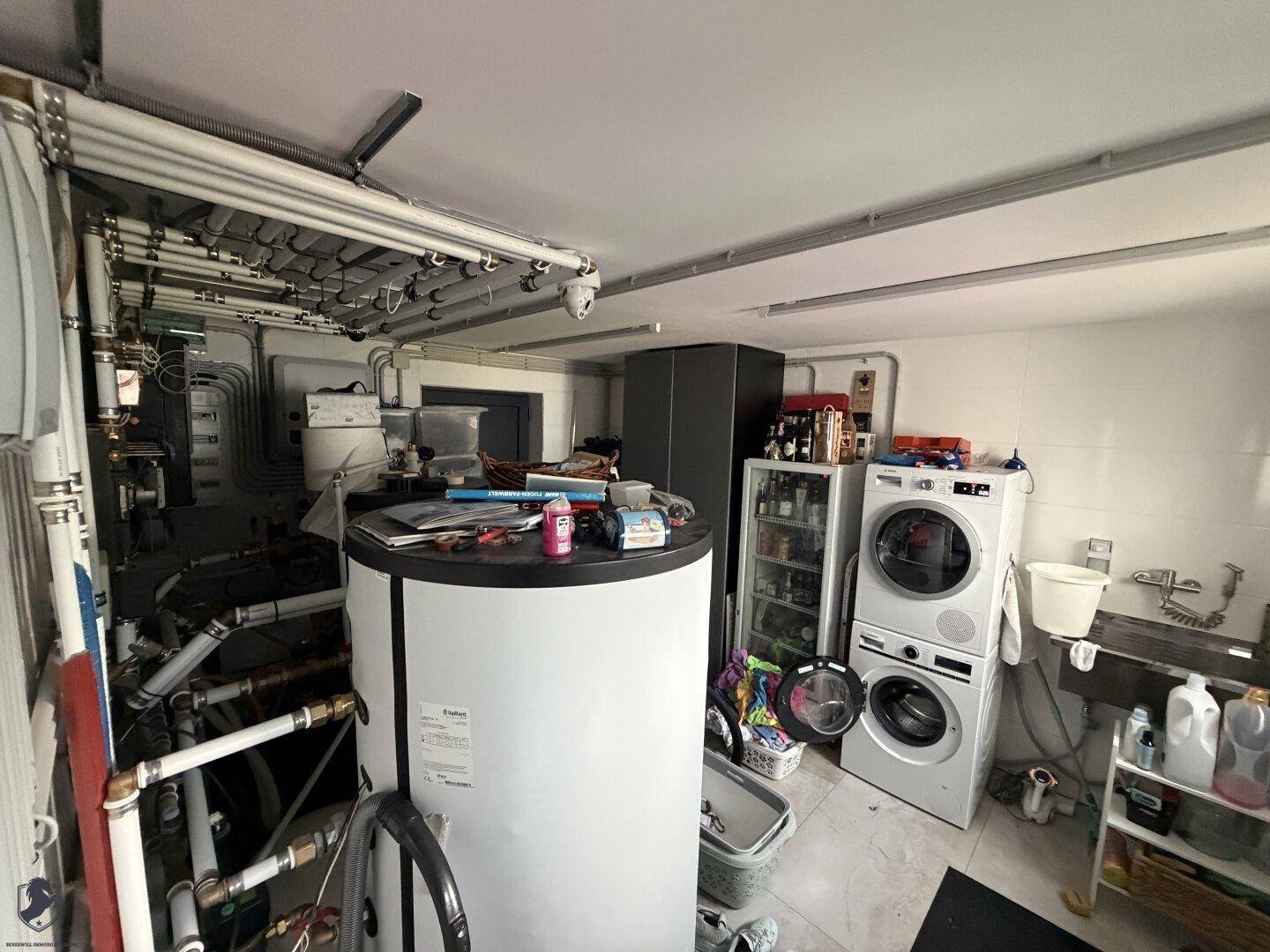 Funktionaler Hauswirtschaftsraum im Keller mit Waschmaschine, Trockner und Warmwasserspeicher.
