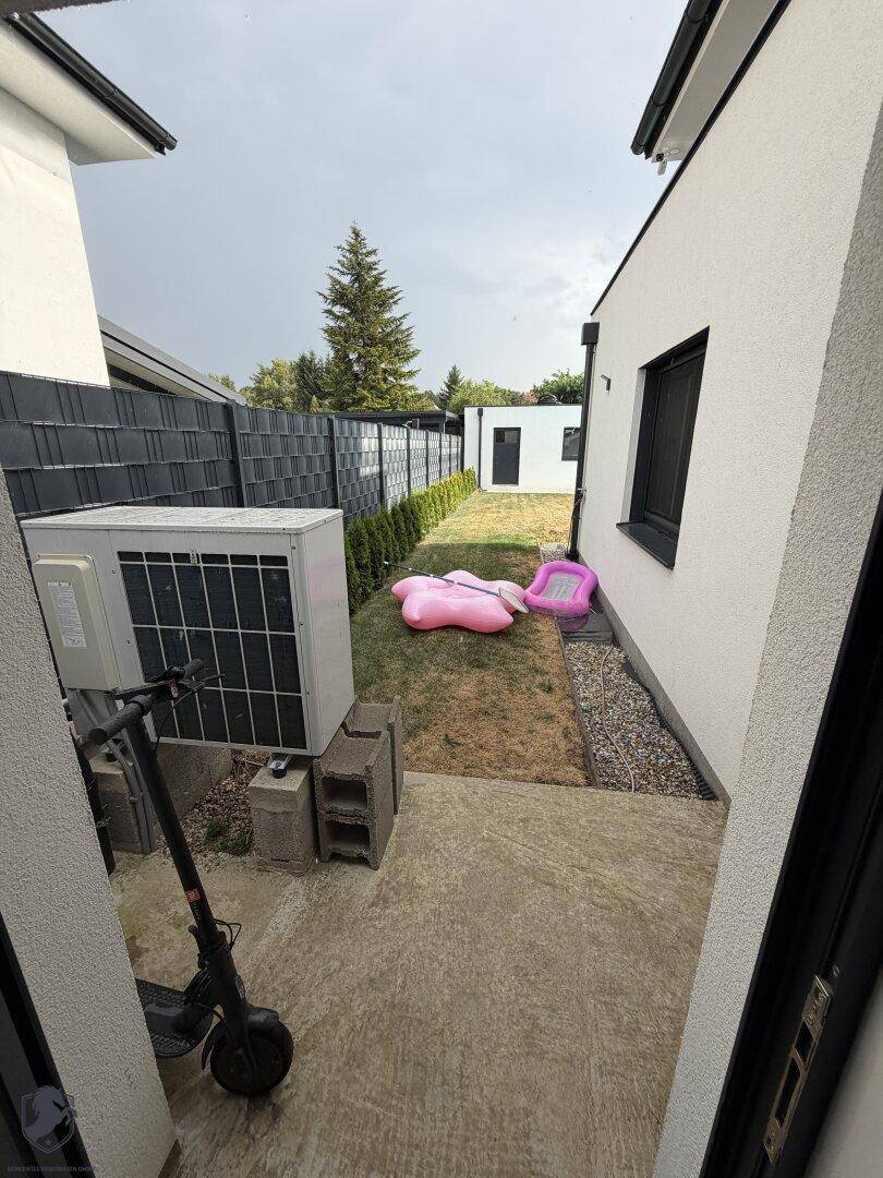 Seitlicher Gartenbereich zwischen den Häusern mit Klimaanlage und einem kleinen Rasenstück.