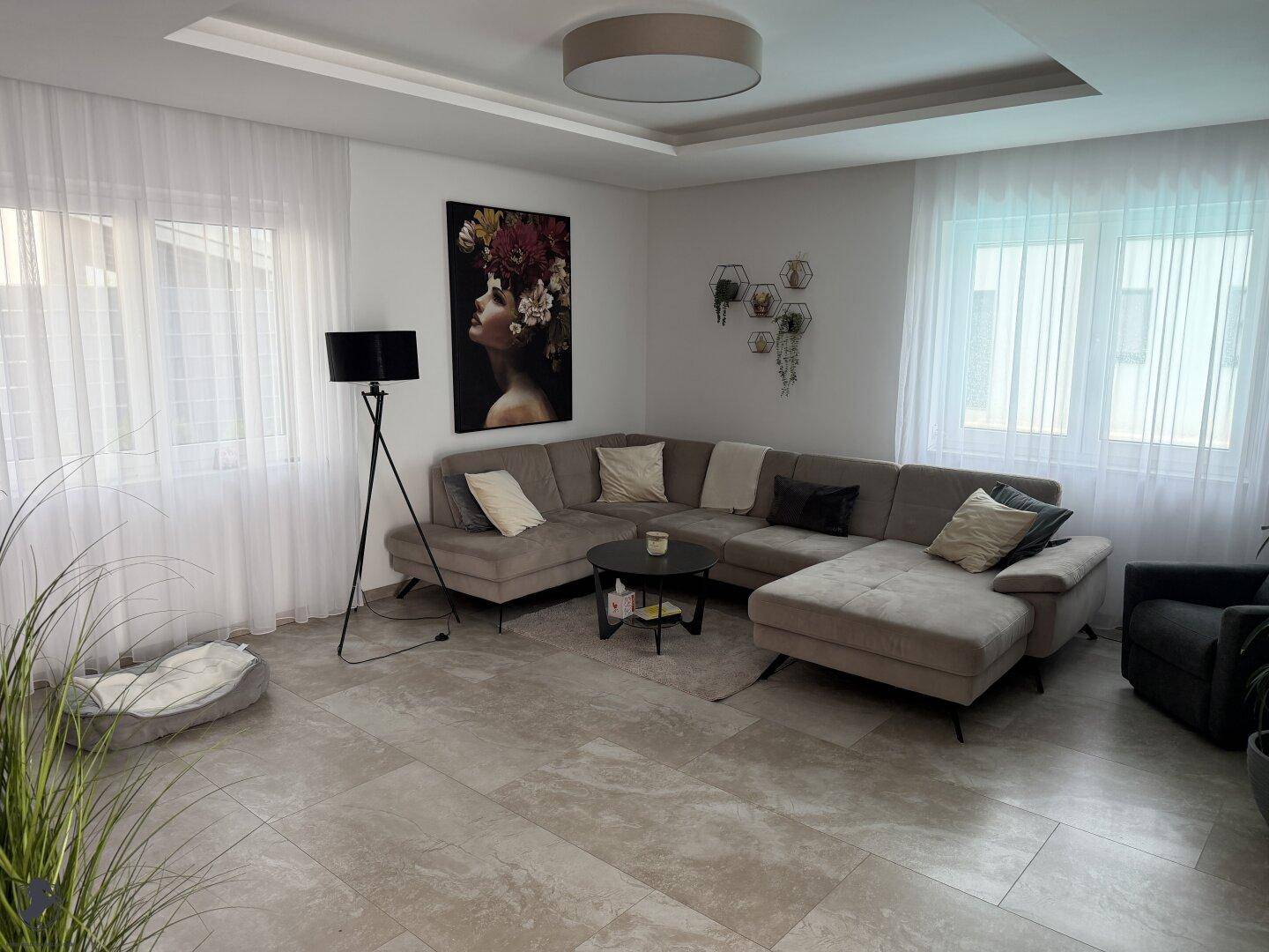 Helles Wohnzimmer mit großem Ecksofa, modernen Fliesen und bodentiefen Fenstern für viel Tageslicht.