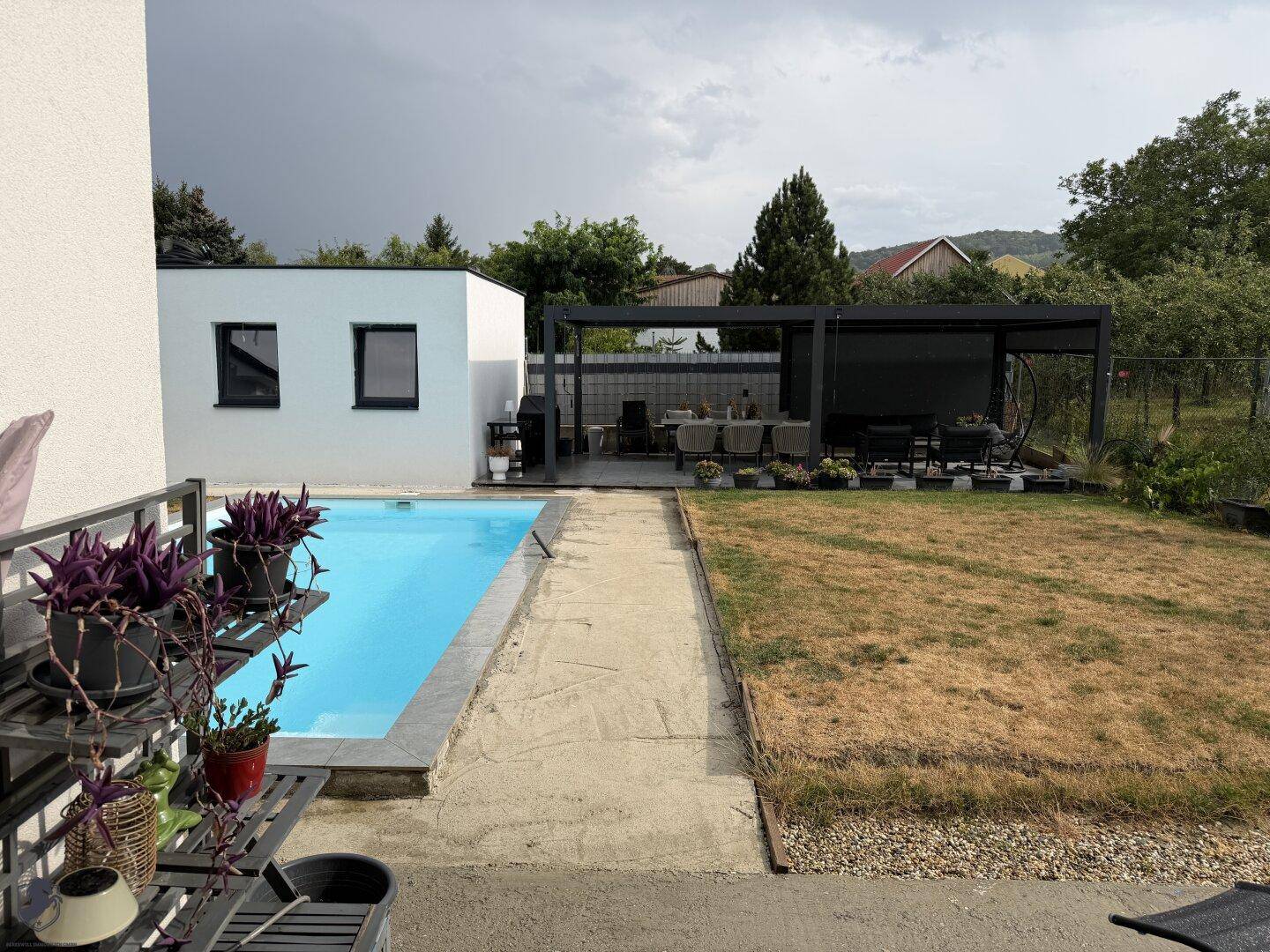 Gartenbereich mit erfrischendem Swimmingpool, gepflastertem Weg und der überdachten Terrasse im Hintergrund.