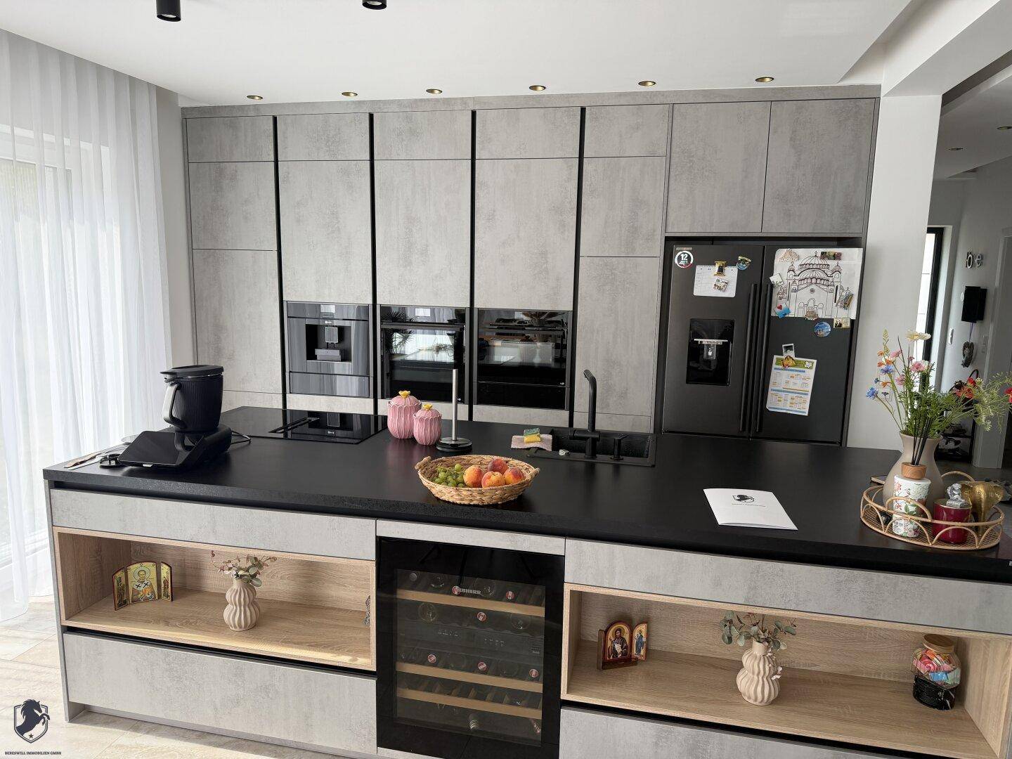 Hochmoderne Küche mit grauen Schränken, schwarzen Arbeitsplatten und integrierten Premium-Geräten.