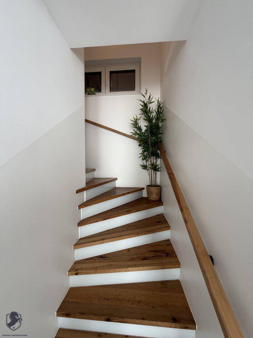 Moderne Holztreppe mit weiß gestrichenen Stufen und einem Fenster, das Tageslicht hereinlässt.