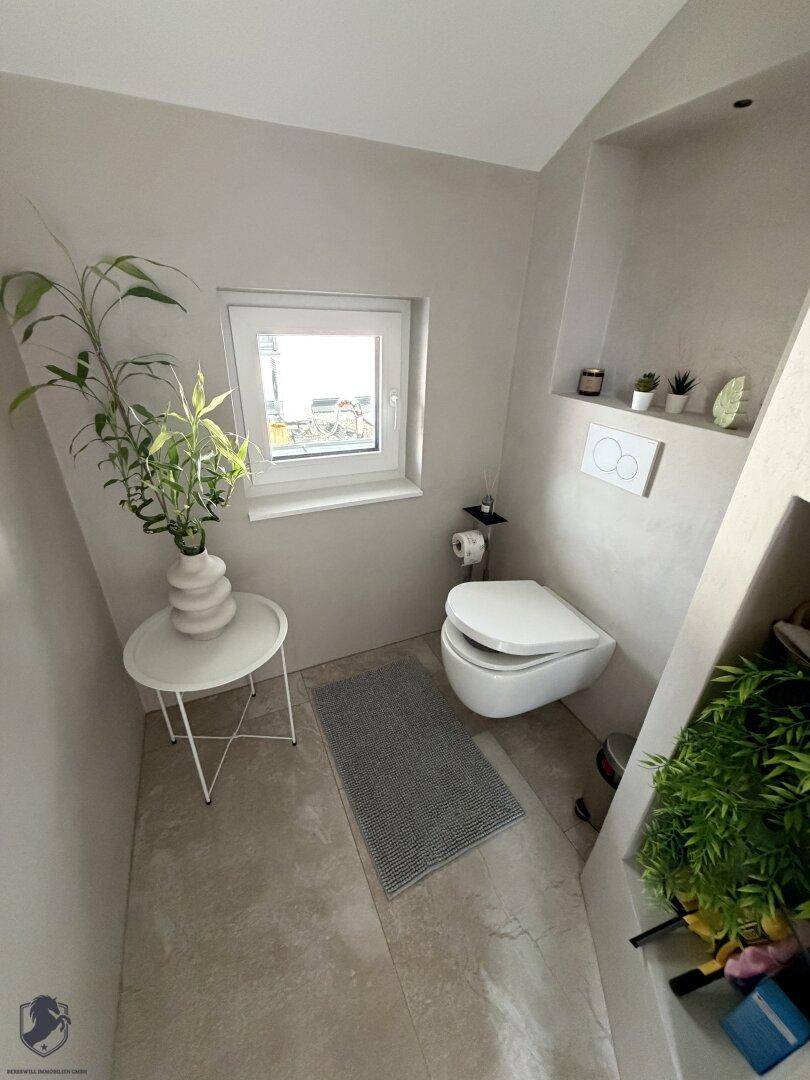 Modernes Gäste-WC mit wandhängendem WC, kleinem Fenster und hellen Fliesen.