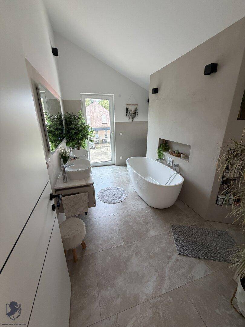Geräumiges Badezimmer mit freistehender Badewanne, Doppelwaschbecken und Zugang zum Außenbereich.