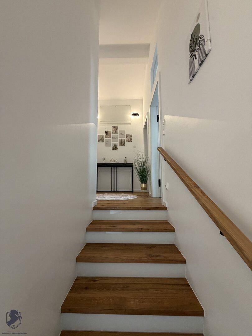 Blick die Holztreppe hinauf zu einem hellen Flur mit dekorativer Konsole und Bildern.