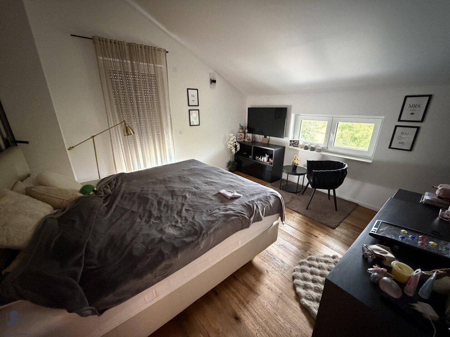 Gemütliches Schlafzimmer mit Holzboden, großem Bett, Fernseher und Fenstern mit Rollos.