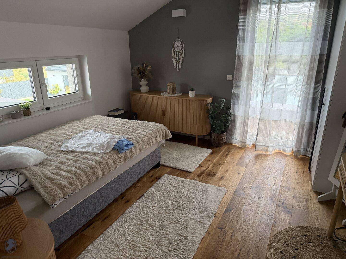 Gemütliches Schlafzimmer mit Holzboden, Dachschräge und großem Fenster für viel Tageslicht.