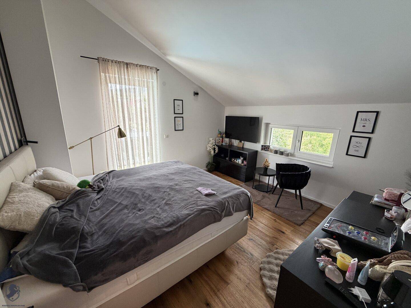 Geräumiges Schlafzimmer im Dachgeschoss mit Holzboden, großem Bett und Medienbereich.