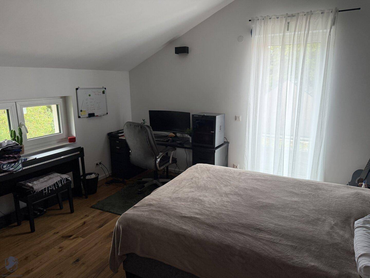 Helles Schlafzimmer mit Arbeitsbereich, Holzboden und Dachschräge, ideal für Home-Office.