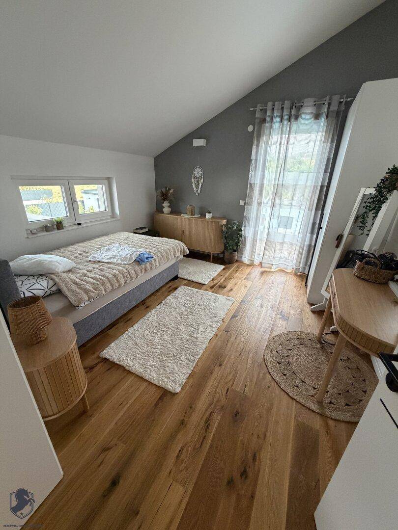 Freundliches Schlafzimmer mit Holzboden, Dachschräge und modernem Beistelltisch.