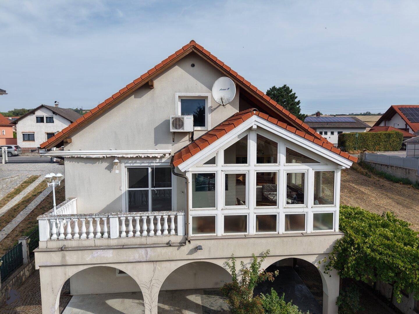 Rückansicht des Hauses mit einem verglasten Wintergarten, Balkon und Satellitenschüssel.