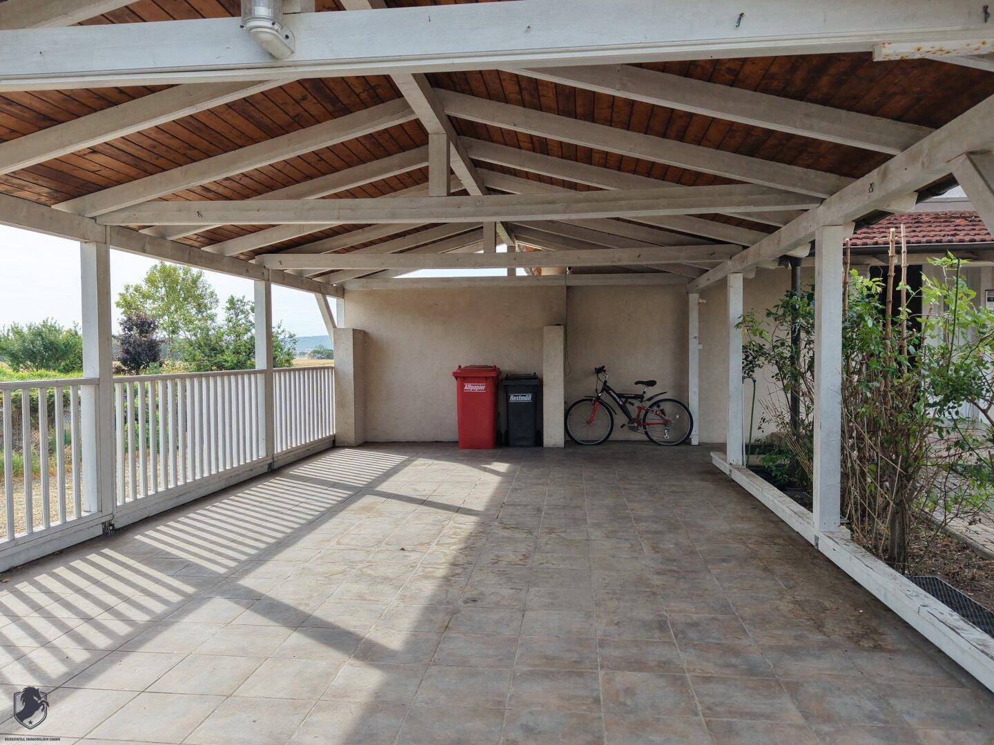 Geräumiger Carport mit Holzdachkonstruktion und Fliesenboden, bietet Platz für Fahrzeuge.
