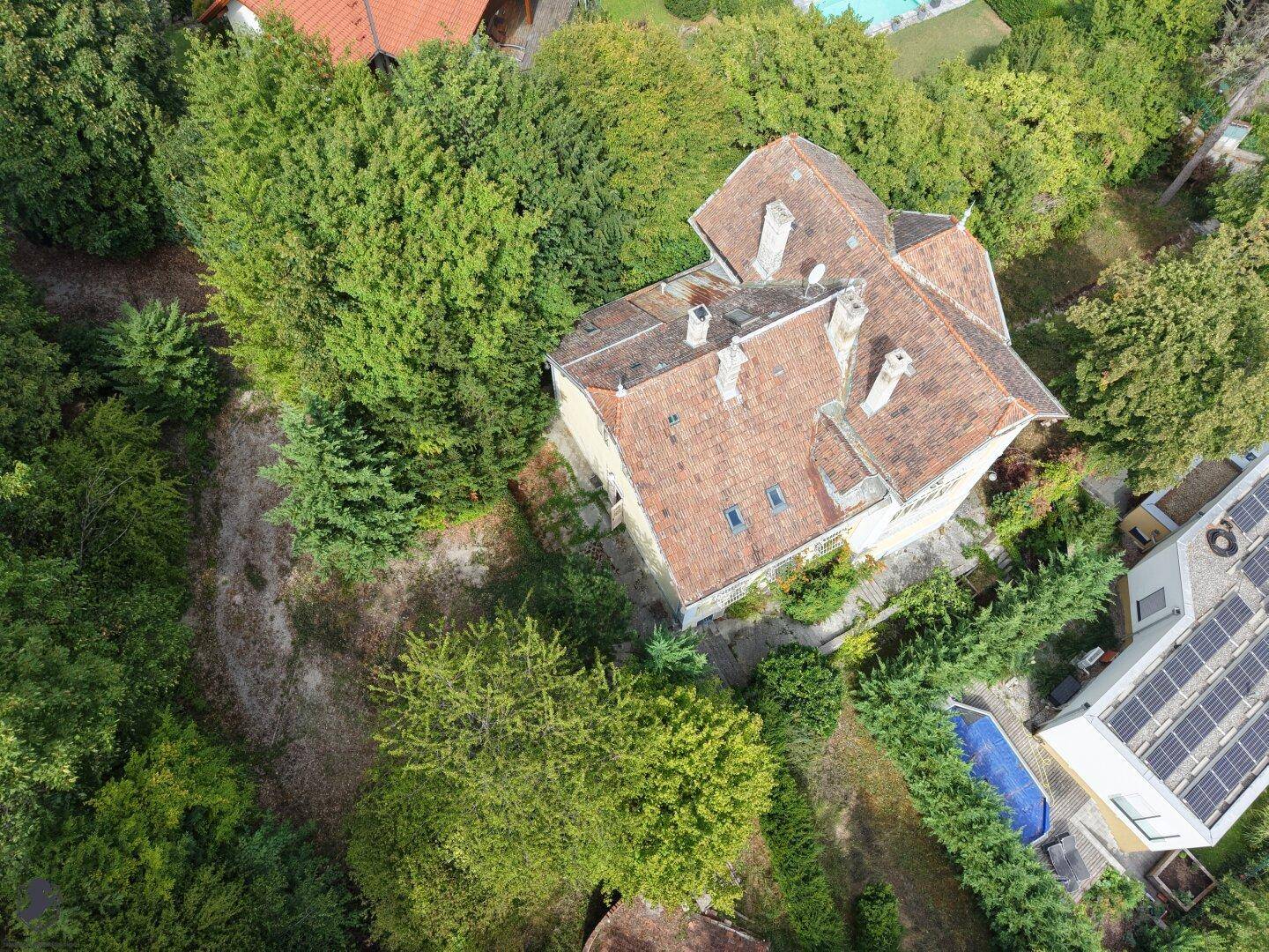 Weitläufige Luftaufnahme der historischen Villa inmitten eines grünen Grundstücks mit Nachbarhäusern.