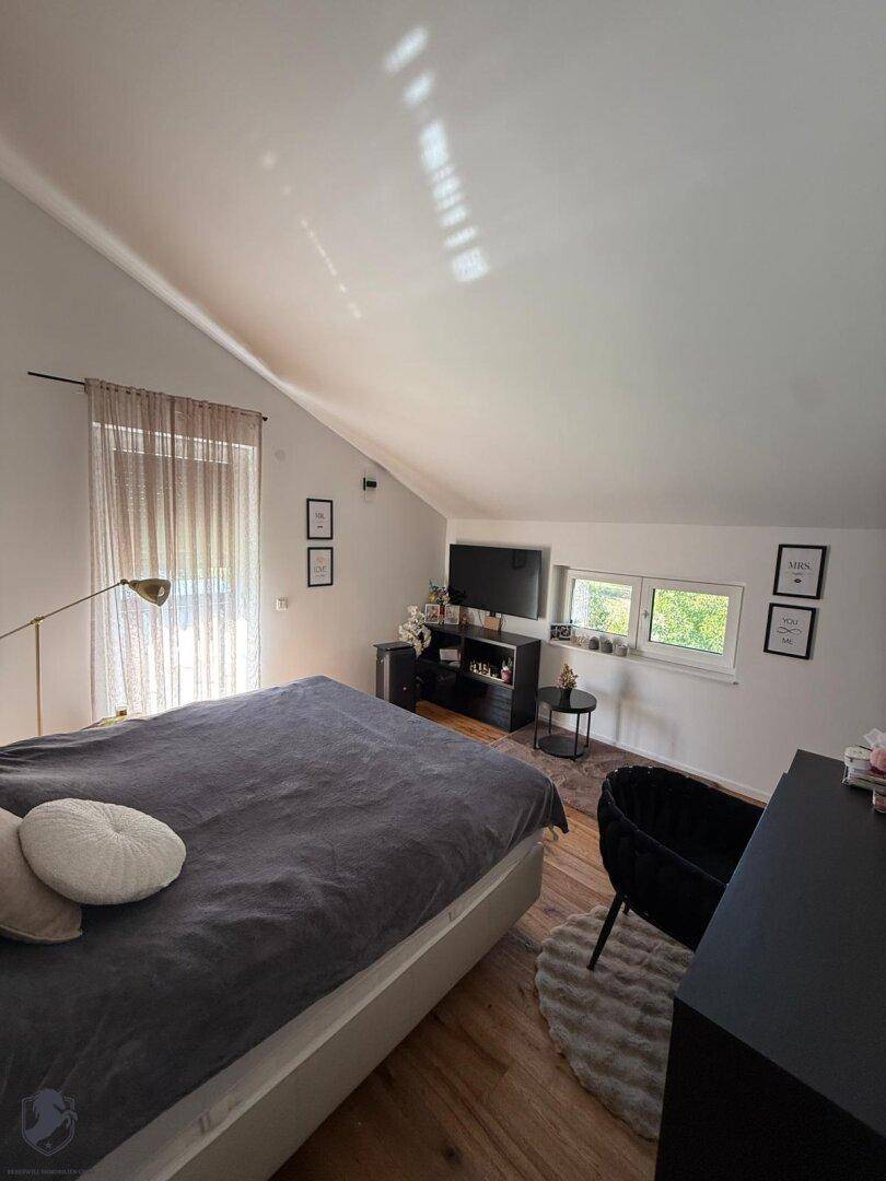 Helles Schlafzimmer im Dachgeschoss mit schräger Decke, Holzboden und großen Fenstern für viel Tageslicht.