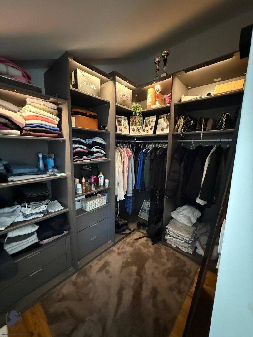Geräumiger begehbarer Kleiderschrank mit maßgefertigten Regalen, Schubladen und integrierter Beleuchtung für optimale Organisation.