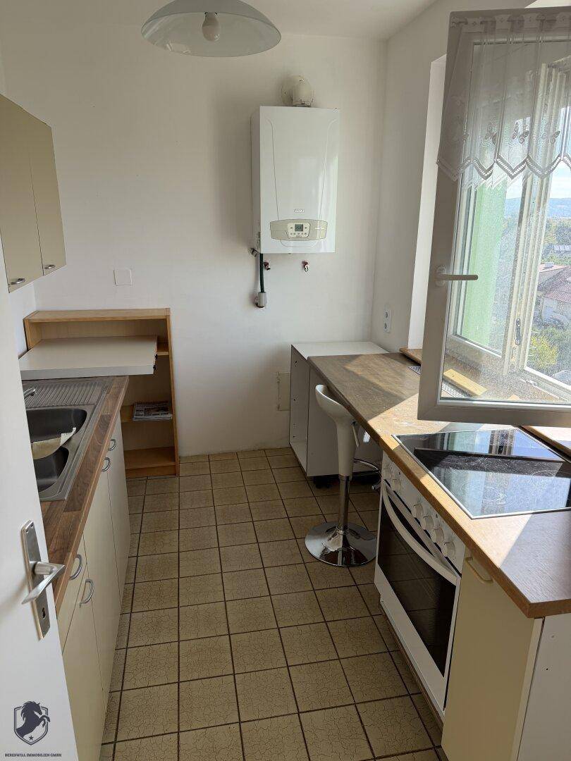 Funktionale Küche mit Fliesenboden, Gastherme und einem kleinen Essbereich am Fenster.