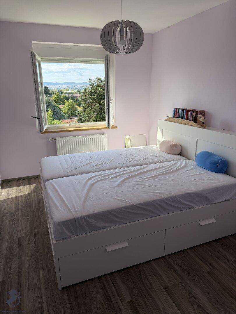 Schlafzimmer mit Laminatboden, Doppelbett und einem Fenster mit schöner Aussicht ins Grüne.