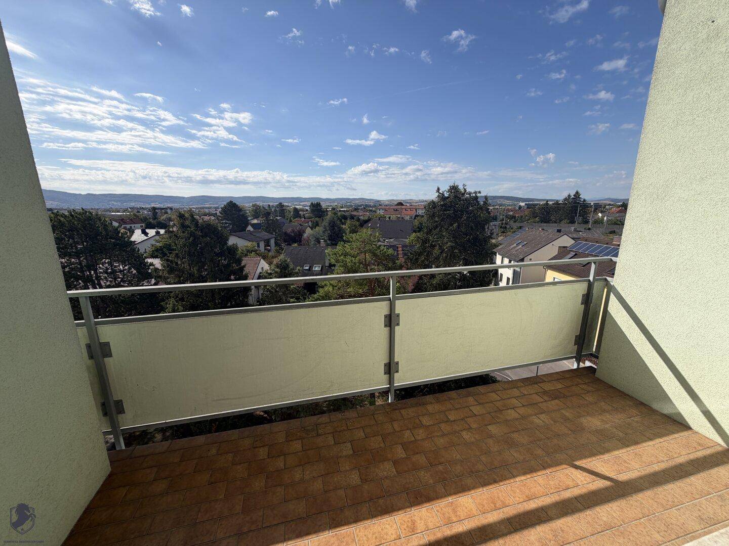 Geräumiger Balkon mit Fliesenboden und weitem Blick über die Stadt und Landschaft.