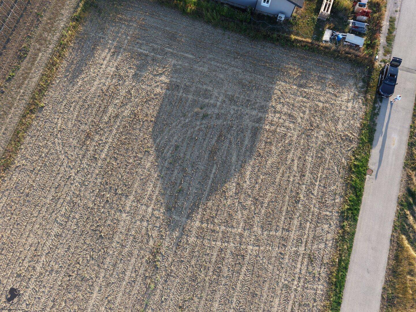 Luftaufnahme eines abgeernteten Feldes mit angrenzender Straße und einem Haus am Rand.