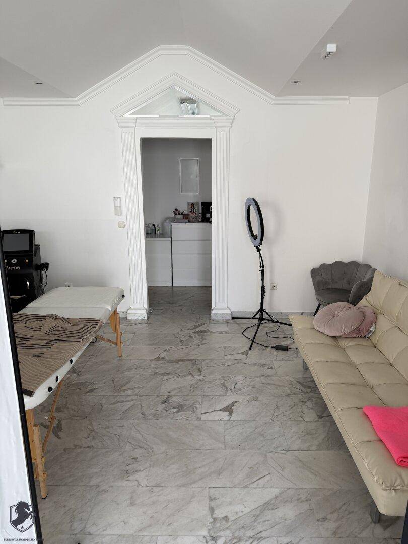Gewerberaum mit dekorativem Türrahmen, Massageliege und beigem Sofa auf Fliesenboden.