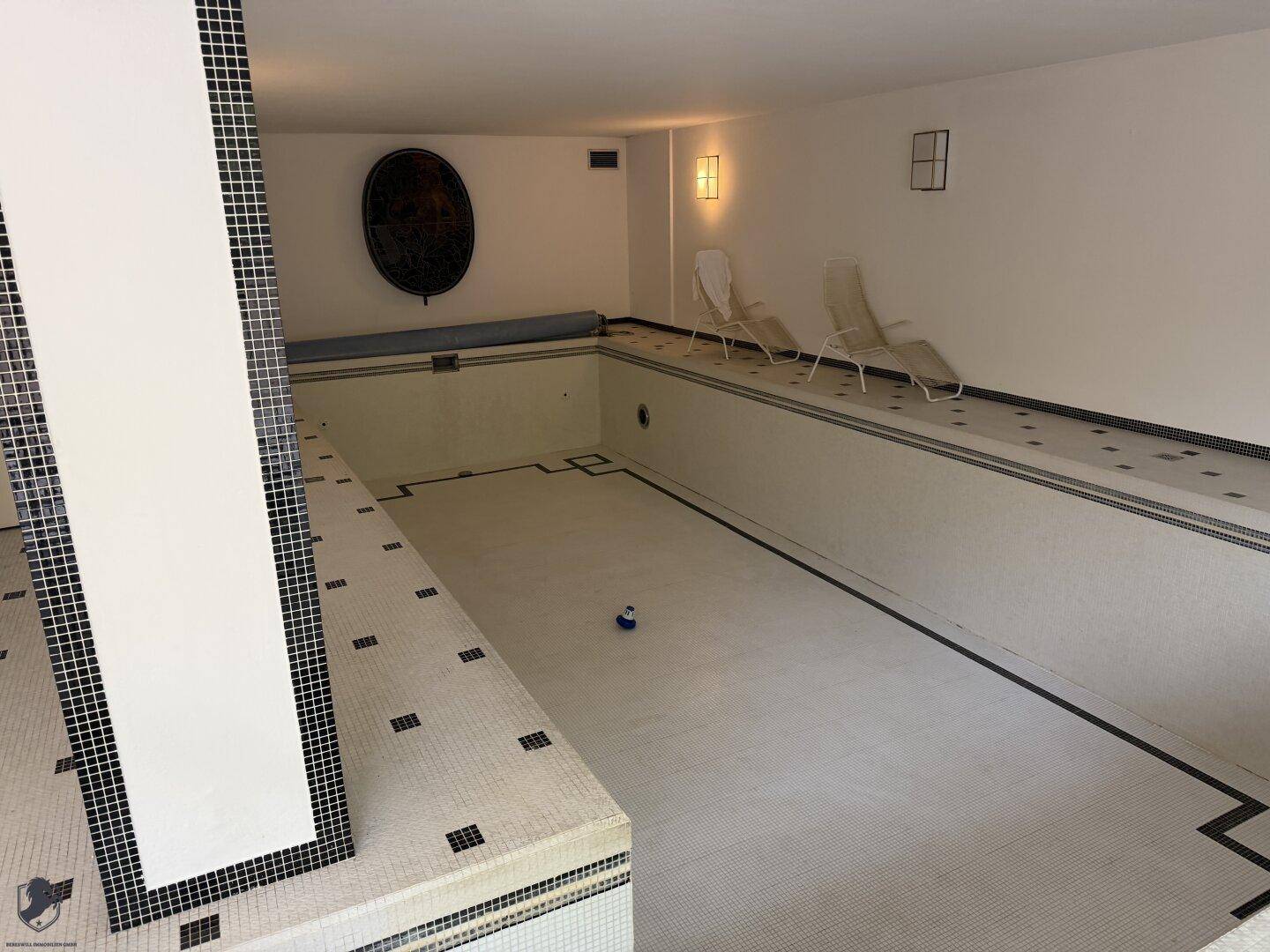 Großer Innenpoolbereich mit Fliesenboden und Liegestühlen, derzeit ohne Wasser.