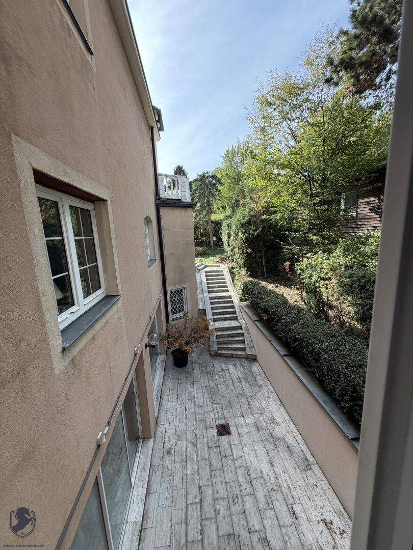 Geräumige Terrasse mit Holzoptik-Fliesen und Treppenzugang zu einem erhöhten Gartenbereich.