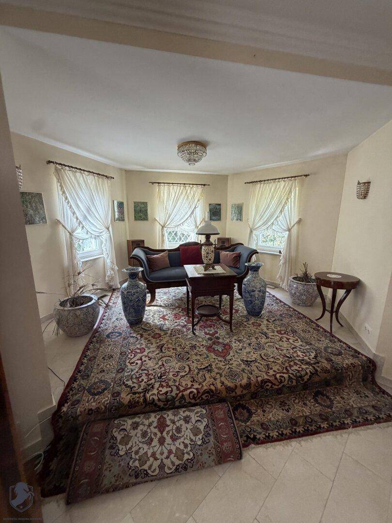 Klassisches Wohnzimmer mit eleganten Möbeln, großem Orientteppich und vielen Fenstern.