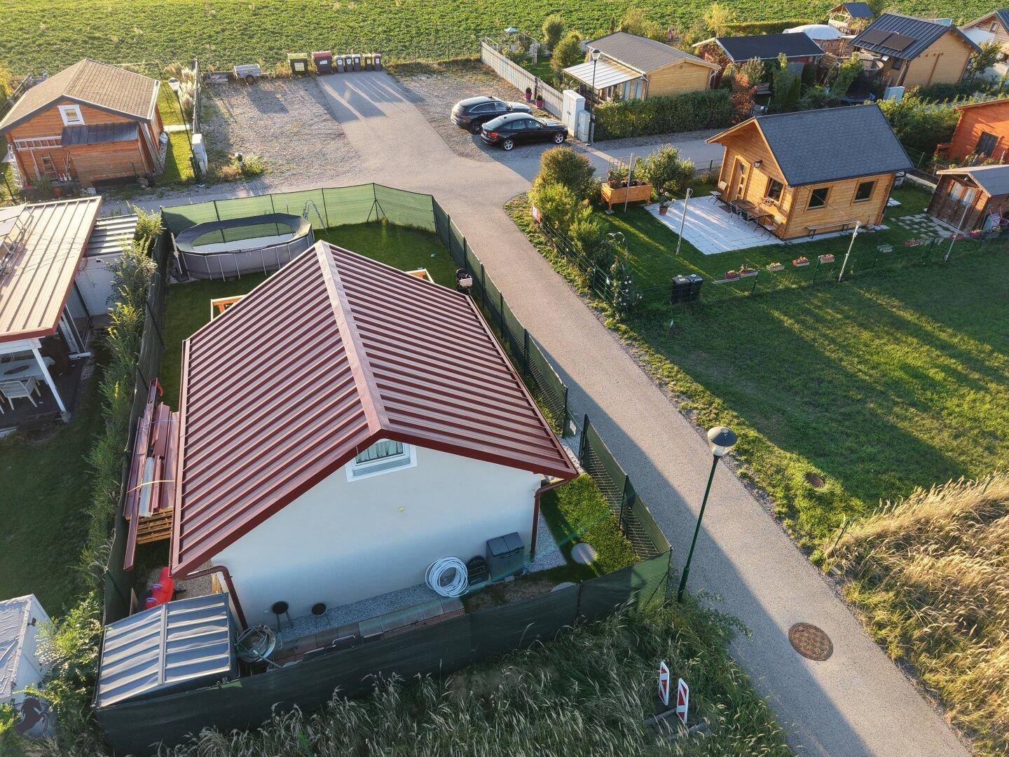 Draufsicht auf das Haus mit rotem Dach, Garten und Trampolin in einer Siedlung.